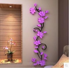 a purple flower is on the wall next to a chair and vase with flowers in it