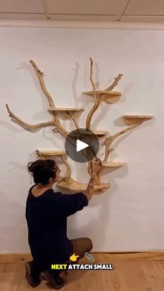 a woman sitting on the floor in front of a tree branch wall hanging with shelves