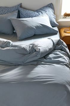 an unmade bed with blue sheets and pillows