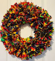 a multicolored wreath hanging on the side of a door with ribbon around it