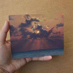 a hand holding up a small piece of art that looks like the sun is setting