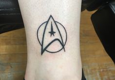 a star trek symbol tattoo on the ankle is shown in black and grey ink,