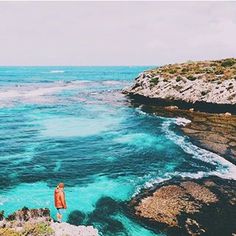 a man standing on the edge of a cliff looking out at the ocean and cliffs