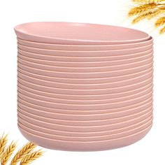 a stack of pink plates sitting on top of a table next to some ears of wheat