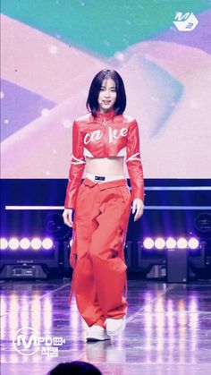 a woman is walking down the runway wearing red pants and a cropped top with white lettering on it