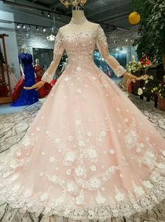 a pink ball gown with long sleeves and flowers on the skirt is displayed in a store