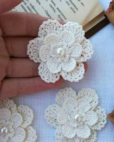 crocheted flowers are being held in front of an open book and some bread