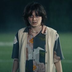 a person standing in front of a soccer field wearing a shirt and vest with flowers on it