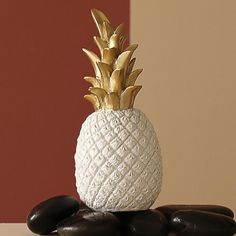 a white pineapple sitting on top of some black rocks next to a red wall