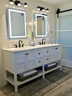 a bathroom with two sinks, mirrors and lights on the wall above them is shown