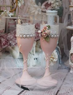 two wine glasses with lace and flowers on them are sitting next to each other in front of a floral arrangement