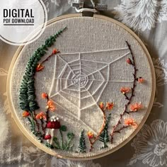 an embroidered spider web surrounded by flowers and plants on a white background with silver hoop