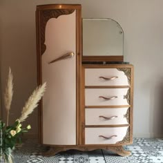 an old fashioned wooden cabinet with drawers and mirror on top, next to a flower vase