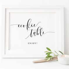 a white framed print with the words cookie table on it next to a cup and candle