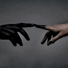 two hands reaching out towards each other with black paint on their fingertipss, against a gray background