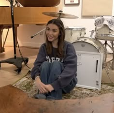 a woman sitting on the floor next to a drum set