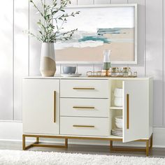 a white and gold sideboard with vases on it in front of a painting