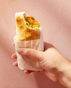 a person holding a sandwich in their hand on a pink surface with a light colored background