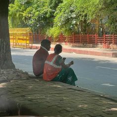 two people sitting on the ground next to a tree