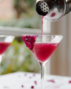 a person pours pink liquid into a martini glass with red sprinkles