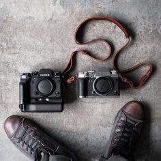 a pair of brown shoes sitting next to two black cameras on top of a cement floor