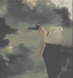 a woman standing on the edge of a cliff with her hair blowing in the wind