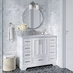 a bathroom with marble walls and flooring, white cabinets and a round mirror on the wall