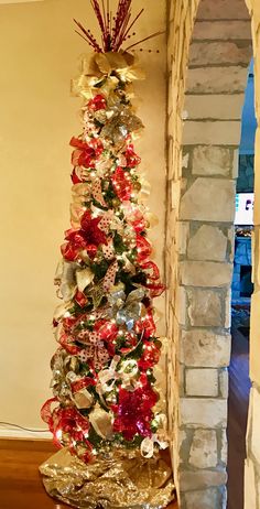 a christmas tree with red and gold ornaments on it in front of a brick wall