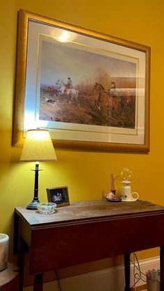 a painting hangs on the wall next to a desk with a lamp and other items