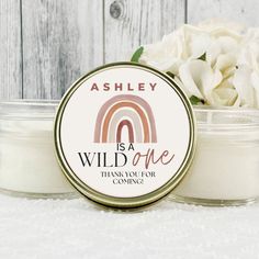 a candle with a rainbow on it next to some white flowers and a wooden background