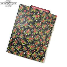 a black notebook with red and green flowers on the cover, sitting on top of a white surface