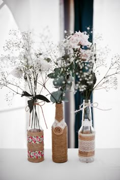 two bottles with flowers in them sitting on a table next to another bottle and vase