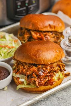 two pulled pork sandwiches with coleslaw and ketchup on a tray in front of an instant pressure cooker