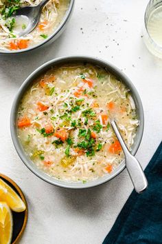 two bowls of chicken noodle soup with lemon slices and parsley on the side