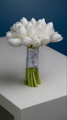 a bouquet of white tulips sitting on top of a table next to a blue wall