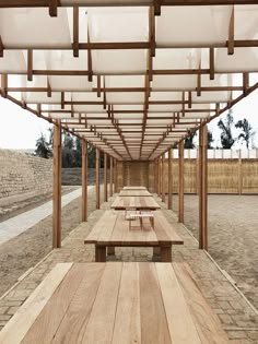 an empty picnic area with wooden benches and pergolated roof