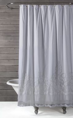 a shower curtain with white lace on the bottom and silver trimmings, in front of a wooden wall