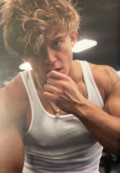 a young man with blonde hair and no shirt is looking at the camera while holding his hand to his mouth