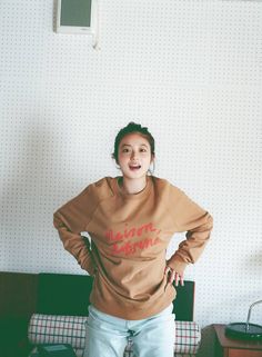 a woman standing in front of a bed wearing a brown sweatshirt with the word'welcome home'on it