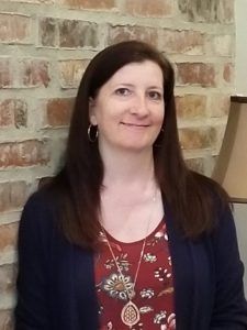 a woman standing in front of a brick wall with a lamp on top of it