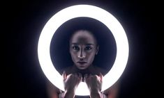 a woman holding a light up in front of her face with both hands and looking at the camera