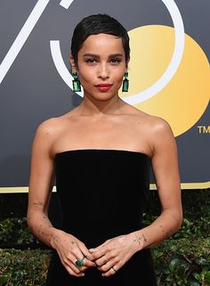 a woman in a black dress with green earrings on her head and one hand under her hip