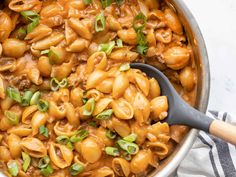 a pot filled with pasta and sauce on top of a white table cloth next to a wooden spoon