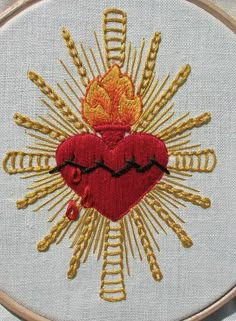 a cross stitched with gold thread and a red heart