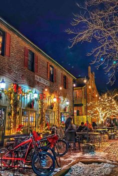 people are sitting at tables in front of christmas lights on the side of an old brick building