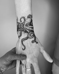 an octopus tattoo on the left arm and wrist is shown in black and white, with two hands holding each other