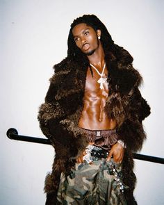 a man with dreadlocks standing in front of a white wall wearing a fur coat