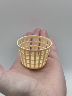 a hand holding a small yellow basket in it's left palm, against a gray background