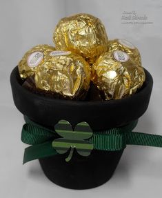 a black pot filled with gold foiled chocolates on top of a green ribbon