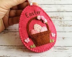 a hand holding a pink felt ornament with an easter basket on it